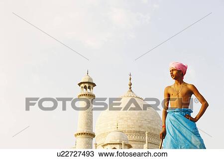 Stock Image - Low angle view of a young man standing in front of a mausoleum, Taj Mahal, Agra, Uttar Pradesh, India. Fotosearch