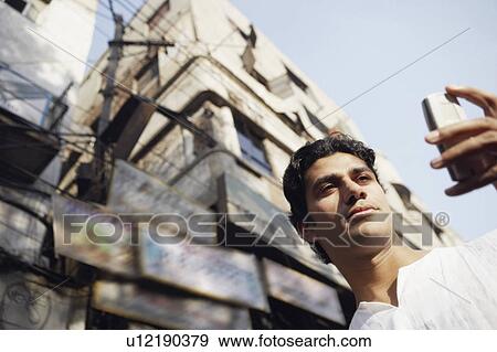 Stock Photo - Low angle view of a young man using a mobile phone. Fotosearch