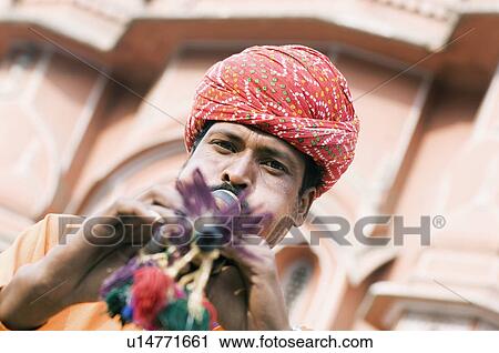 Stock Image - Portrait of a snake charmer playing a flute in front of a palace, Hawa Mahal, Jaipur, Rajasthan, India. Fotosearch