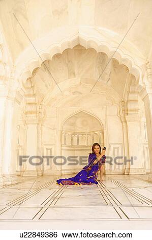 Stock Photograph - Young woman sitting on the floor and holding a hand mirror. Fotosearch