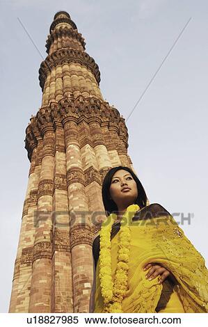 Stock Photography - Low angle view of a young woman standing in front of a monument, Qutub Minar, New Delhi, India. Fotosearch