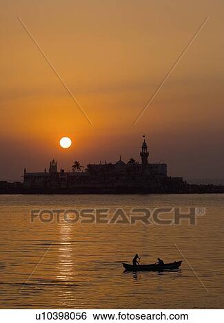 Stock Photograph - Silhouette of two people on a boat in the sea with a mosque in the background, Haji Ali Dargah, Mumbai, Maharashtra, India. Fotosearch