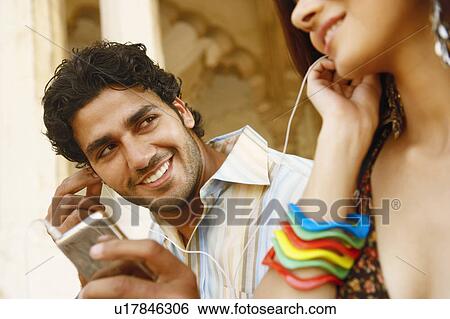 Stock Photograph - Close-up of a young couple listening to music on headphones, Agra Fort, Agra, Uttar Pradesh, India. Fotosearch