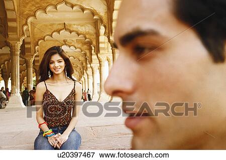 Stock Photo - Close-up of a young man smiling with a young woman sitting behind him, Agra Fort, Agra, Uttar Pradesh, India. Fotosearch