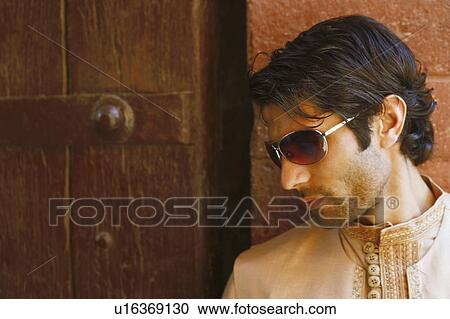 Stock Image - Close-up of a young man standing in front of a wooden door, Agra Fort, Agra, Uttar Pradesh, India. Fotosearch