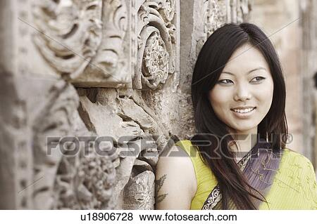 Close-up of a young woman standing beside a carved wall and smiling View Large Photo Image Stock Photo - Close-up of a young woman standing beside a carved wall and smiling. Fotosearch