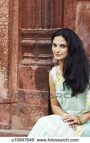 Stock Photo - Portrait of a young woman sitting in a front of a column. Fotosearch