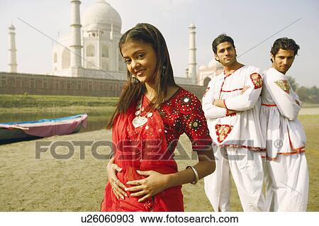 Stock Image - Portrait of a young woman smiling with two young men standing behind her on the riverbank, Taj Mahal, Agra, Uttar Pradesh, India. Fotosearch
