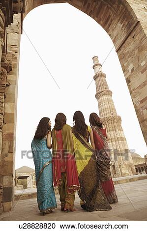 Stock Image - Rear view of four women standing together in front of a monument, Qutub Minar, New Delhi, India. Fotosearch