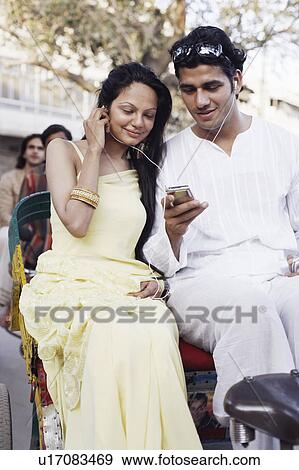 Young couple sitting in a rickshaw and listening to an MP3 player View Large Photo Image Stock Photo - Young couple sitting in a rickshaw and listening to an MP3 player. Fotosearch