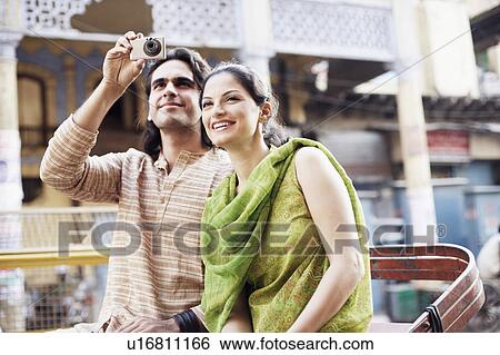Stock Photograph - Young couple sitting in a rickshaw and taking a photograph. Fotosearch