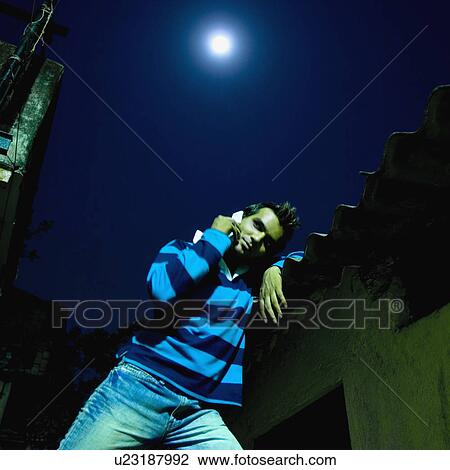 Stock Image - Low angle view of a young man talking on a mobile phone, Mumbai, Maharashtra, India. Fotosearch