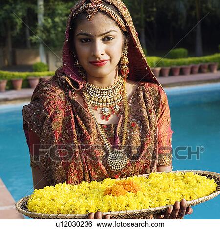 Stock Photograph - Portrait of a bride holding a tray of flower garlands in a traditional wedding dress . Fotosearch