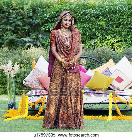 Stock Photography - Portrait of a bride in a traditional wedding dress standing in front of a bed on the lawn. Fotosearch