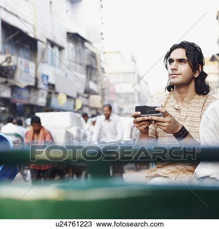 Stock Image - Young man sitting in a rickshaw and holding a mobile phone. Fotosearch