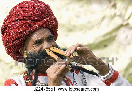 Stock Image - Close-up of a mature man playing two flutes with his nose, Jaipur, Rajasthan, India. Fotosearch
