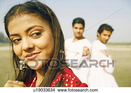 Picture - Close-up of a young woman smiling with two young men standing behind her. Fotosearch