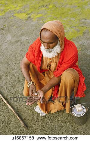 Stock Photo - High angle view of a priest rubbing tobacco in his palm, Agra, Uttar Pradesh, India. Fotosearch
