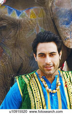 Stock Image - Portrait of a young man standing with an elephant. Fotosearch