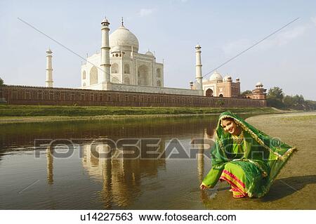 Stock Image - Young woman crouching on the riverbank, Taj Mahal, Agra, Uttar Pradesh, India. Fotosearch