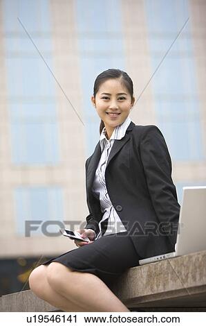 Business woman sitting beside laptop with cell phone in her hand View Large Photo Image Stock Image - Business woman sitting beside laptop with cell phone in her hand. Fotosearch
