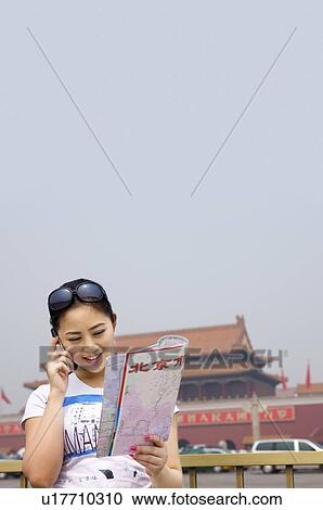Stock Image - Young woman on the phone holding a map in her hand. Fotosearch