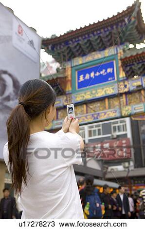 Stock Image - Young woman photographing at wangfujing snack street. Fotosearch