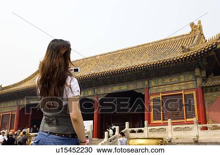 Stock Image - Young woman taking photograph at Forbidden City. Fotosearch