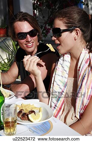 Stock Image - Young couple eating at restaurant table. Fotosearch