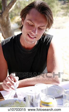 Stock Photography - Young man eating at restaurant table. Fotosearch
