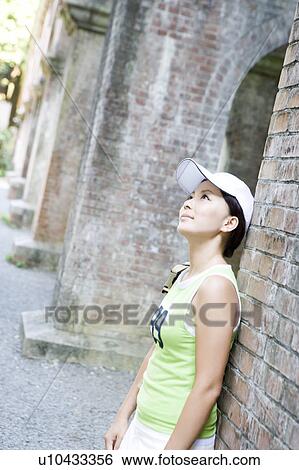 A young woman standing against brick wall View Large Photo Image Stock Photograph - A young woman standing against brick wall. Fotosearch