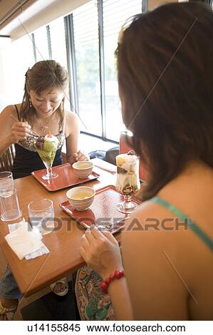 Stock Photography - Two young women eating ice cream in coffee shop. Fotosearch