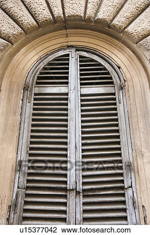 Stock Image - Close-up of wooden shutters and arched window in Rome, Italy.. Fotosearch
