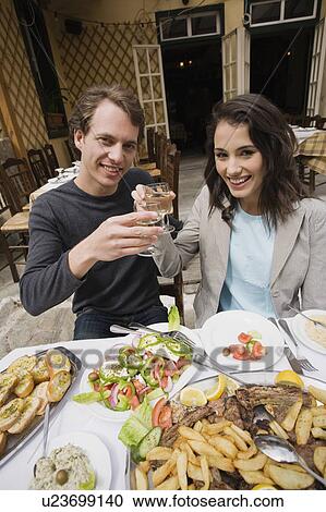 Stock Image - Couple toasting at a table with Greek food. Fotosearch