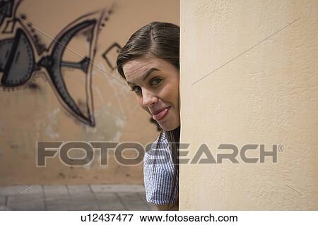 Stock Photo - Woman looking from behind a wall, tongue stuck out. Fotosearch