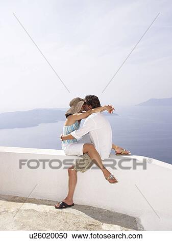 Stock Image - Couple kissing on a low wall, sea view. Fotosearch