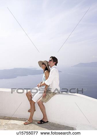Stock Photo - Couple leaning on a low wall, sea view. Fotosearch