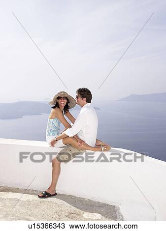 Stock Image - Couple sitting on a low wall, sea view. Fotosearch