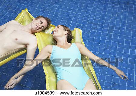 Stock Image - Couple lying on lylos holding hands.. Fotosearch