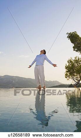 Stock Photo - Man stands in open space sky and reflective pool arms out.. Fotosearch