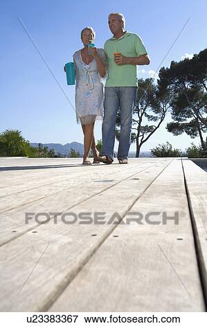 Stock Photo - Older couple carrying drinks on terrace.. Fotosearch