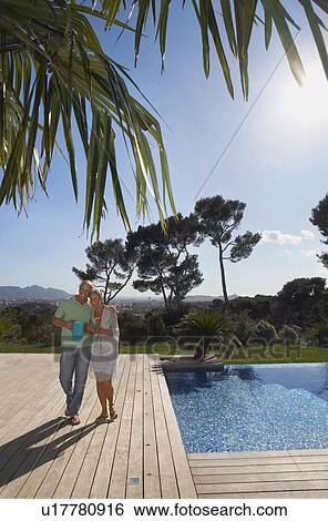 Stock Photograph - Older couple carrying drinks on terrace.. Fotosearch