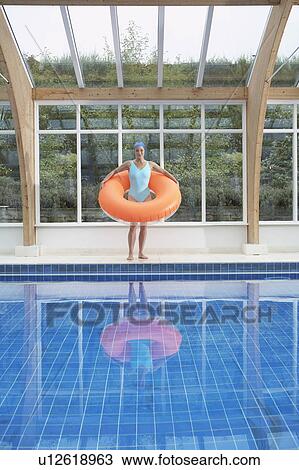 Stock Image - Woman standing with rubber ring by pool.. Fotosearch