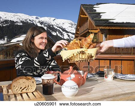 Stock Image - Young woman having breakfast on terrace. Fotosearch