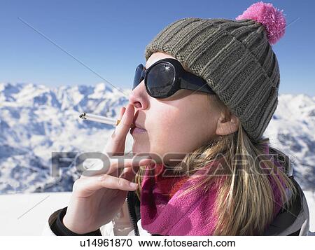 Stock Image - Young woman smoking in snow gear. Fotosearch