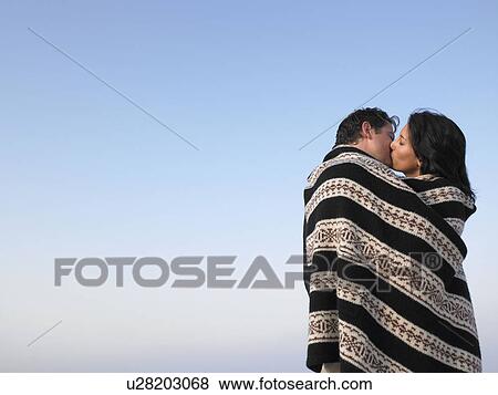 Stock Photo - Couple wrapped in a cover, kissing. Fotosearch