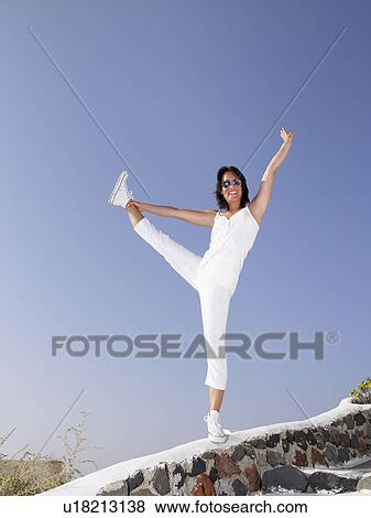 Woman holding her leg, on a low wall View Large Photo Image Stock Photo - Woman holding her leg, on a low wall. Fotosearch