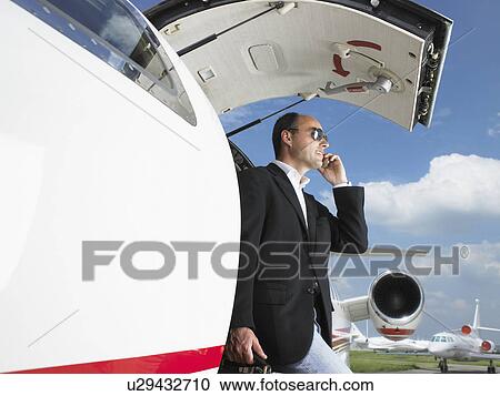 Stock Image - Businessman exiting private jet while on cell phone.. Fotosearch