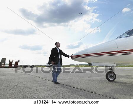 Picture - Businessman touching nose of private jet on tarmac.. Fotosearch