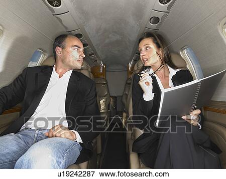 Businesswoman and businessman seated inside a private jet having a discussion. View Large Photo Image Stock Photo - Businesswoman and businessman seated inside a private jet having a discussion.. Fotosearch
